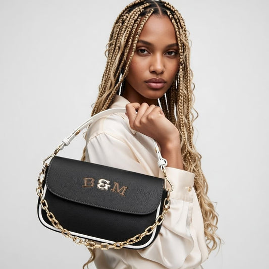 Woman holding a black handbag with gold chain detail and 'B&M' monogram on a light gray background